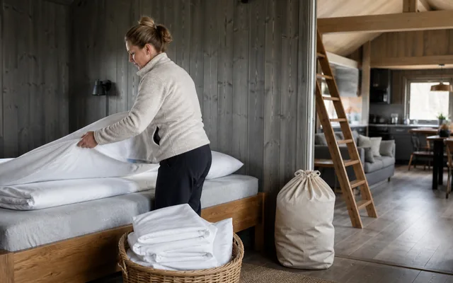 Renholder legger rent sengetøy på en seng i en norsk utleiehytte før neste gjest.